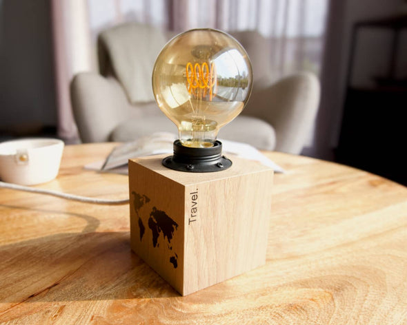 Lampe à poser contemporaine tendance cube en bois avec inscription travel et carte du monde sur table basse